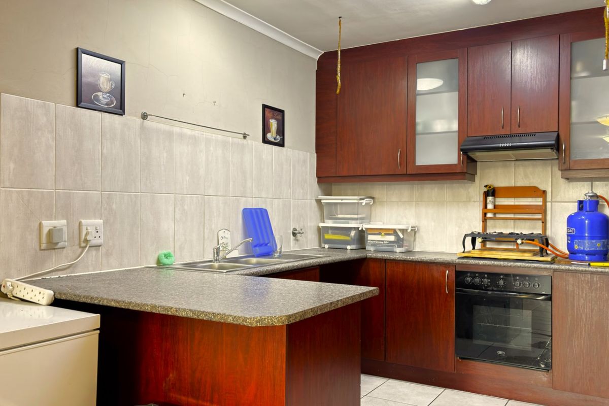 A functional kitchen featuring dark wood-look cabinetry, laminate countertops, a built-in oven, and a tiled backsplash with a double sink.