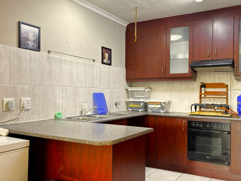A functional kitchen featuring dark wood-look cabinetry, laminate countertops, a built-in oven, and a tiled backsplash with a double sink.