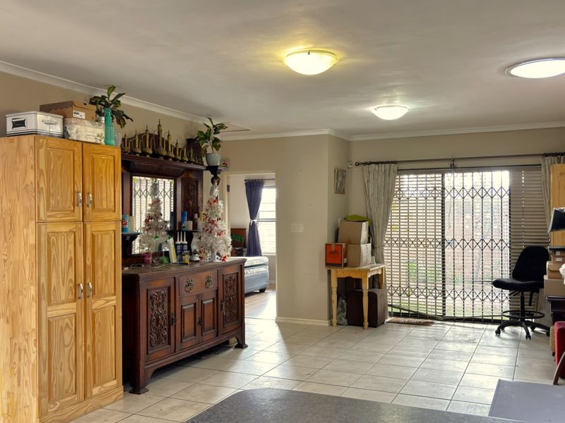 Spacious living area featuring tiled flooring, ceiling lighting, and a sliding glass door with security gate providing access to the exterior.