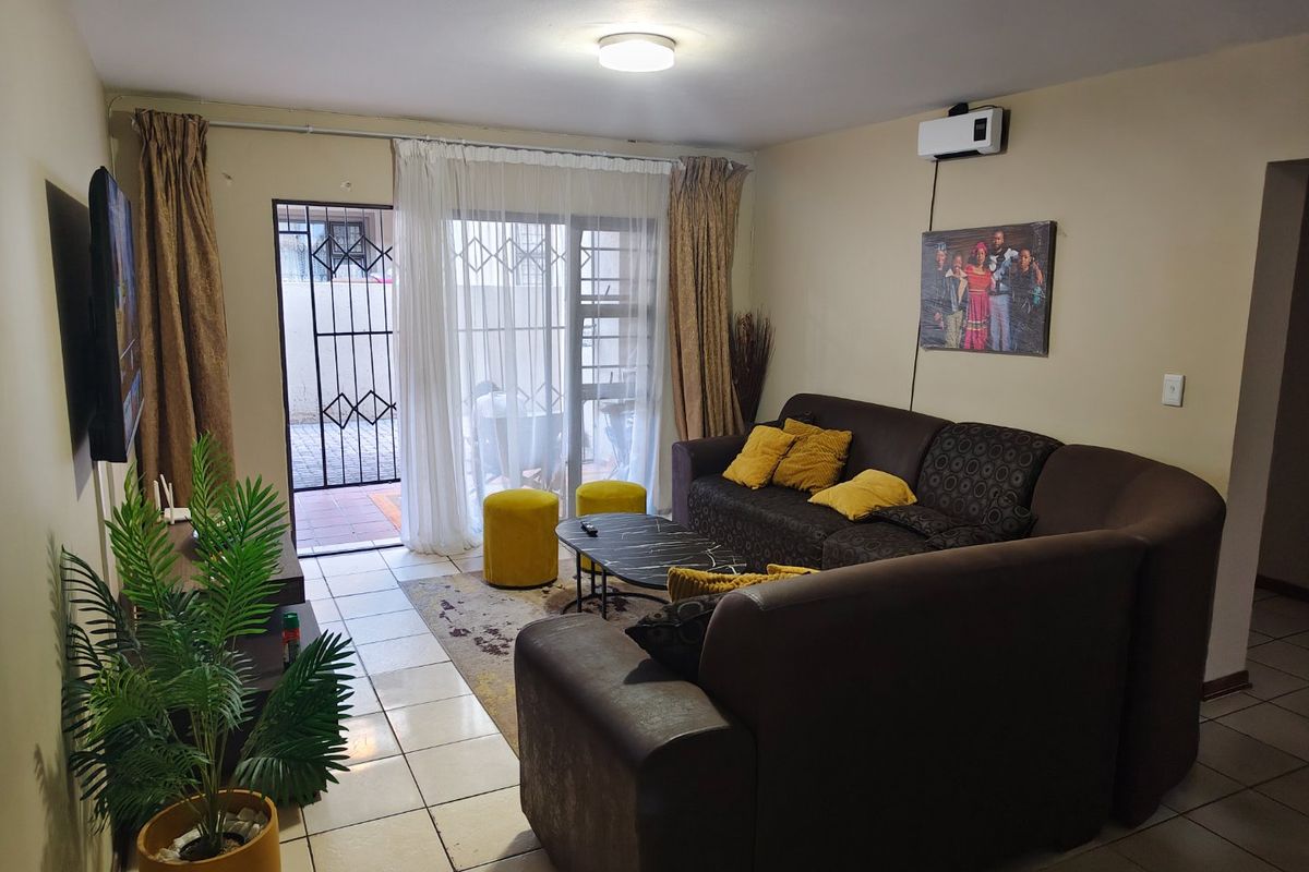 A living room featuring tiled flooring, a wall-mounted air conditioning unit, and a sliding glass door leading to an outdoor area with a security gate.