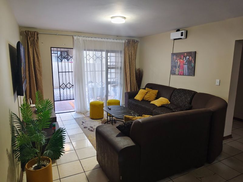 A living room featuring tiled flooring, a wall-mounted air conditioning unit, and a sliding glass door leading to an outdoor area with a security gate.