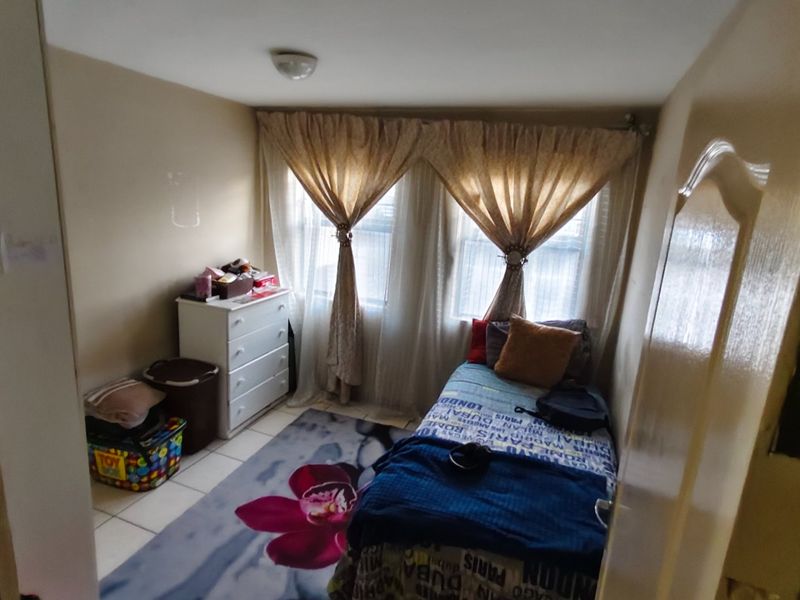 A compact bedroom featuring tiled flooring and natural light through dual windows.