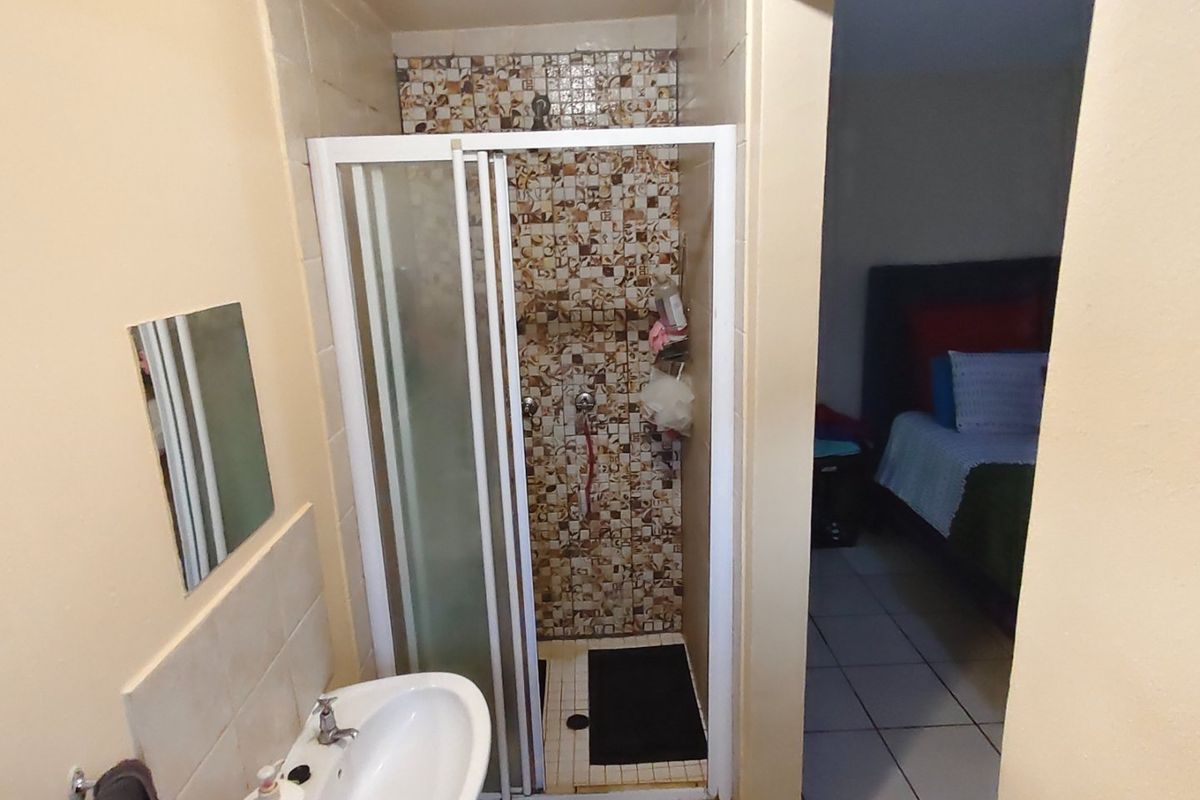 A compact bathroom featuring a shower enclosure with mosaic tiling and a pedestal basin, adjacent to a bedroom area.
