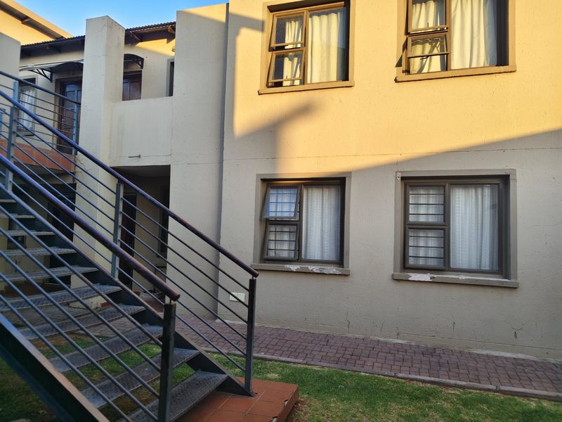 Exterior view of an apartment building featuring a metal staircase, paved walkway, and aluminium window frames with security bars.