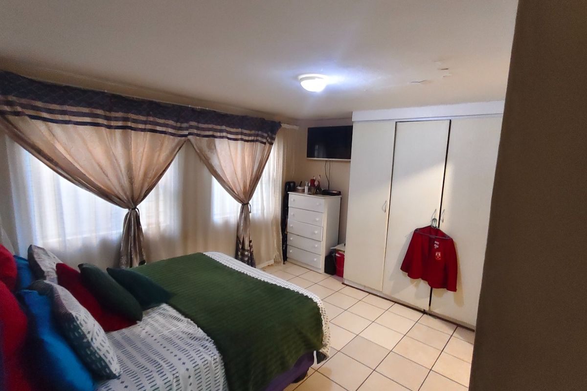 A bedroom featuring tiled flooring and built-in cupboards, with visible ceiling water staining requiring attention.