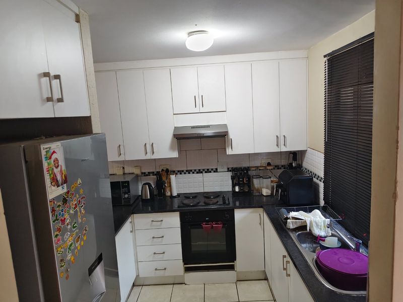 A compact kitchen featuring white cabinetry, black granite countertops, a built-in oven with hob, and a stainless steel sink with tiled backsplash.