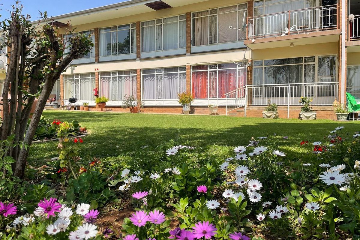 Rear view of the apartment building featuring a well-maintained garden, brick facade, and private balconies with metal railings.