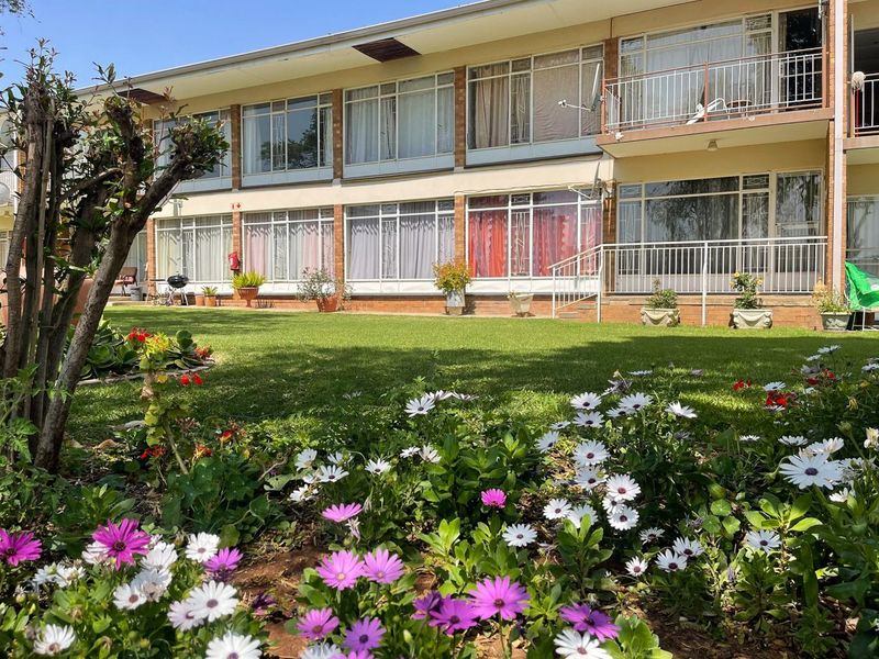 Rear view of the apartment building featuring a well-maintained garden, brick facade, and private balconies with metal railings.