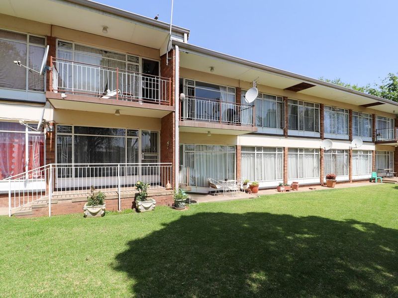 Rear view of a multi-story apartment building featuring brick facade, private balconies, and access to a shared garden area.