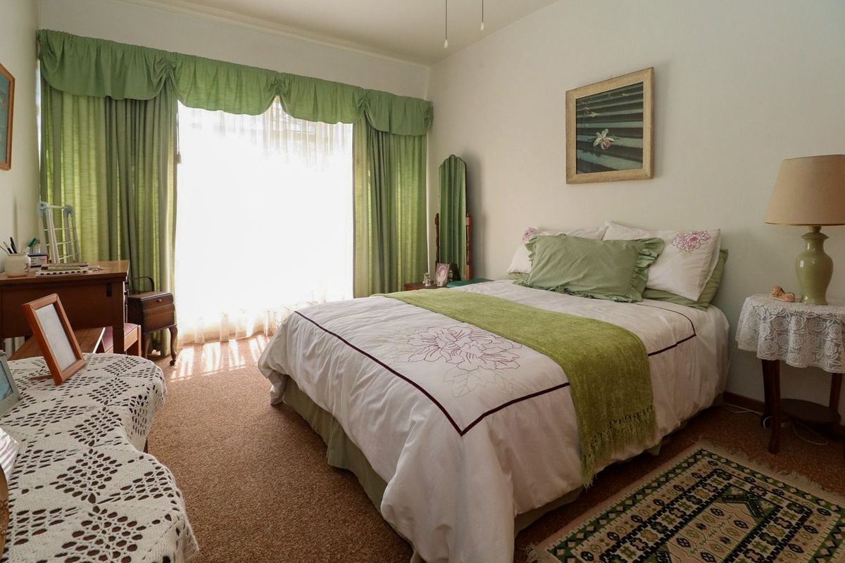 A bedroom featuring carpeted flooring and large windows with curtain treatments, offering a functional space with potential for modernization.