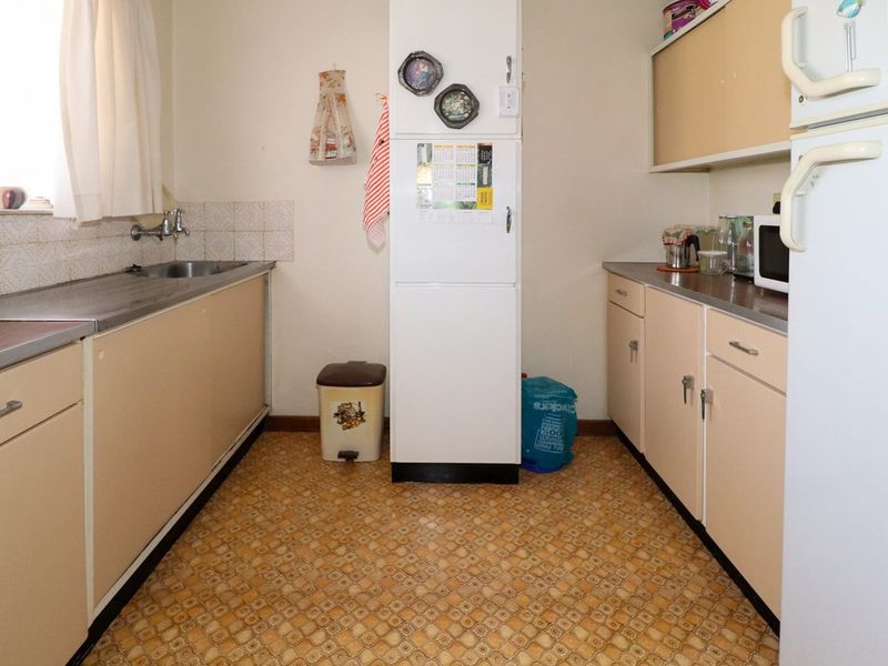 A functional galley-style kitchen featuring original cabinetry, laminate countertops, and a stainless steel sink, offering significant potential for a modern renovation.