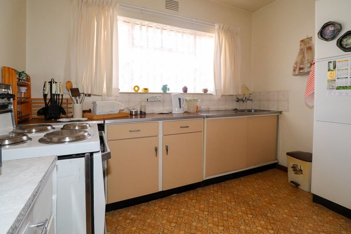 A dated kitchen featuring original cabinetry, a stainless steel sink, tiled splashback, and an electric stove, offering significant potential for modernization.