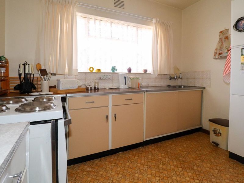 A dated kitchen featuring original cabinetry, a stainless steel sink, tiled splashback, and an electric stove, offering significant potential for modernization.