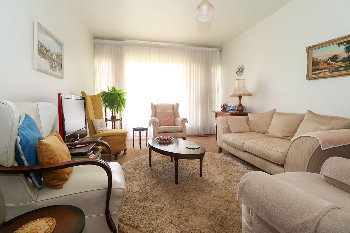 A comfortable living room featuring neutral walls, carpeted flooring, and a large window allowing for ample natural light.