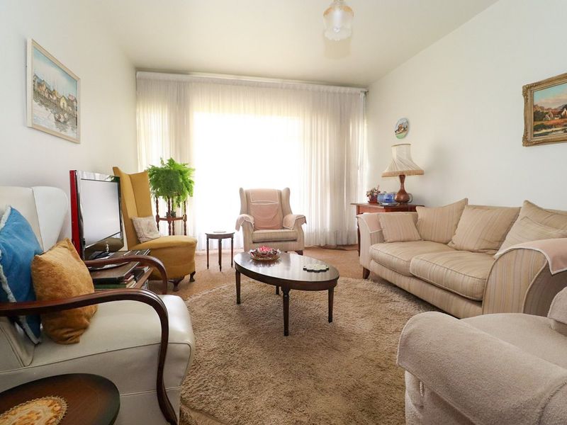A comfortable living room featuring neutral walls, carpeted flooring, and a large window allowing for ample natural light.