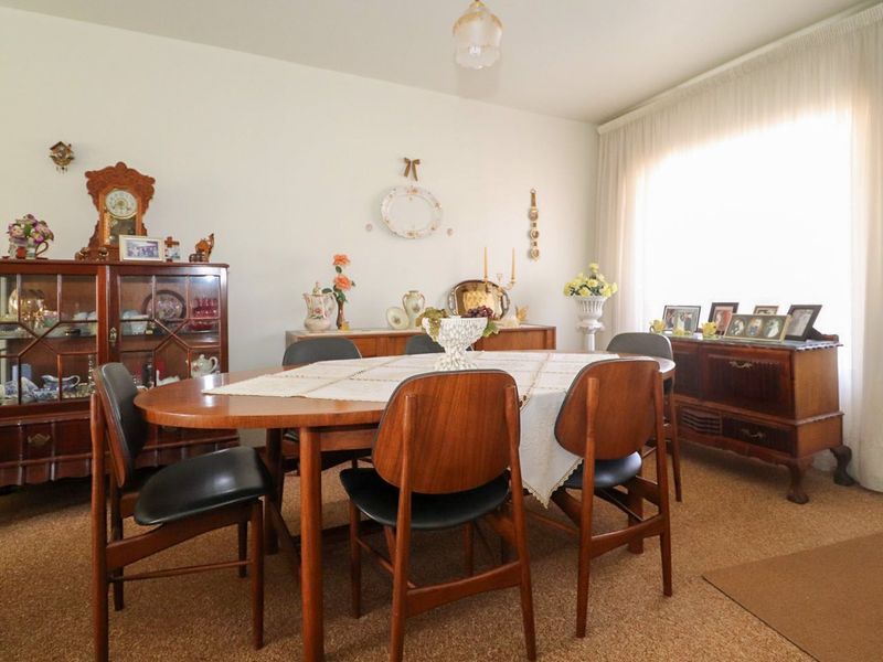 A traditional dining room featuring carpeted flooring and large windows with curtains, offering a functional space for family meals.