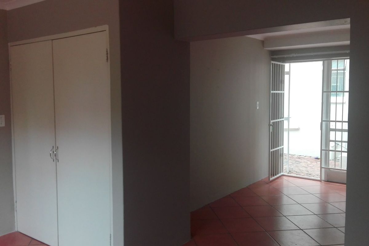 An empty living area featuring tiled flooring, a built-in cupboard, and direct access to an outdoor space through a security gate and glass door.