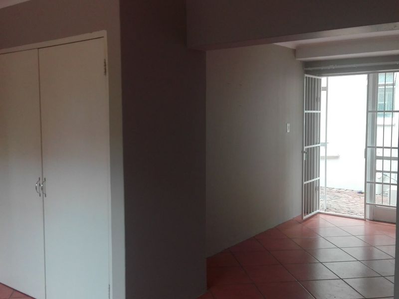 An empty living area featuring tiled flooring, a built-in cupboard, and direct access to an outdoor space through a security gate and glass door.