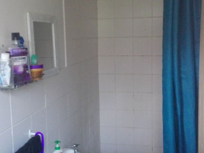 A functional bathroom featuring a wall-mounted basin, tiled walls, and a shower area with a curtain rail, requiring some cosmetic updates.