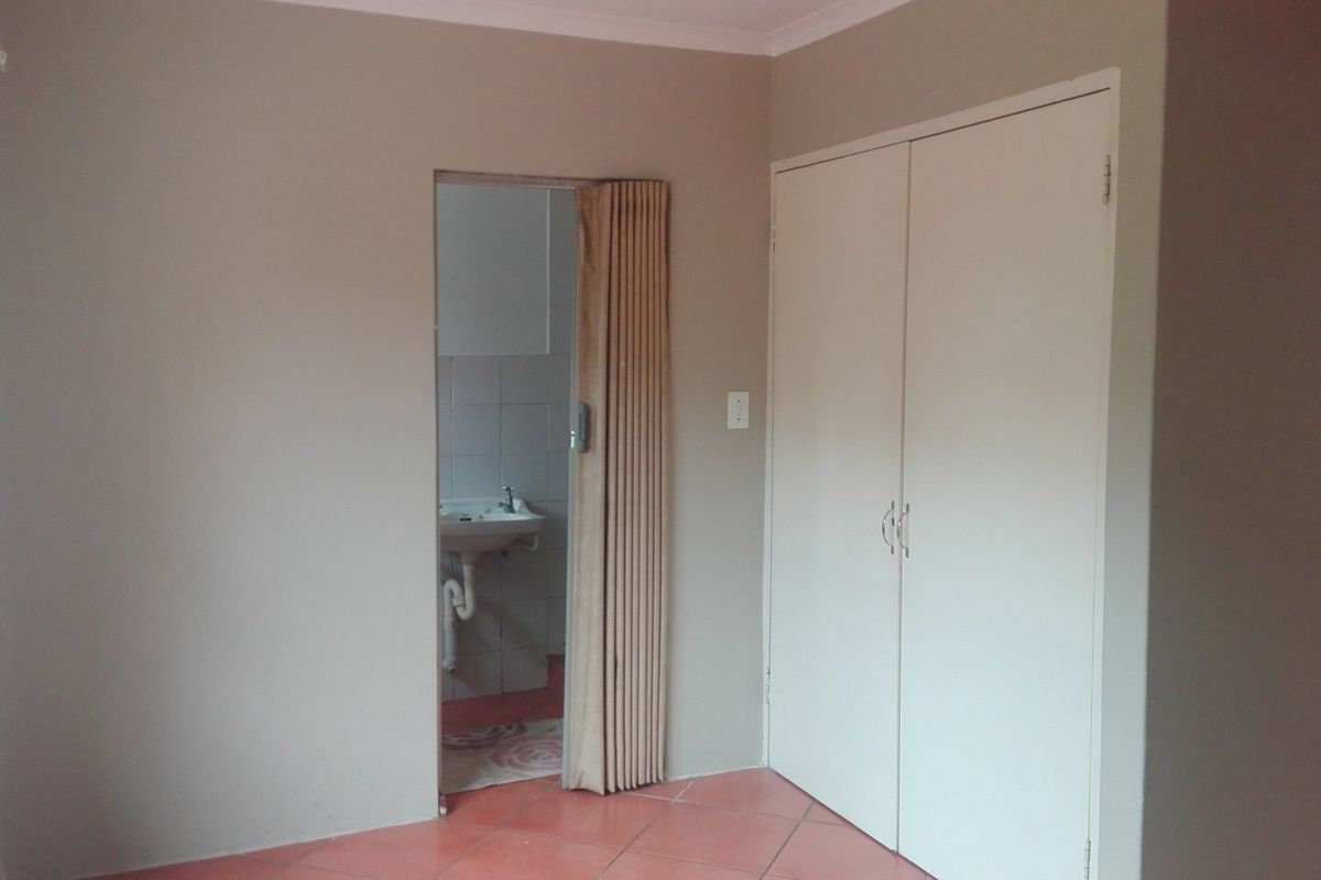 An empty bedroom featuring built-in wardrobes, tiled flooring, and a folding door leading to an en-suite bathroom area.