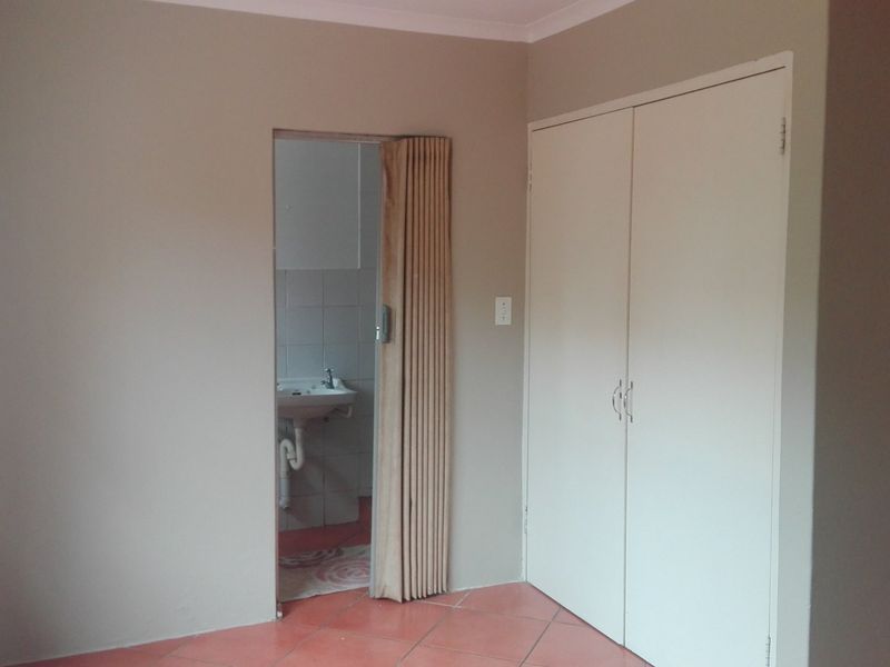 An empty bedroom featuring built-in wardrobes, tiled flooring, and a folding door leading to an en-suite bathroom area.