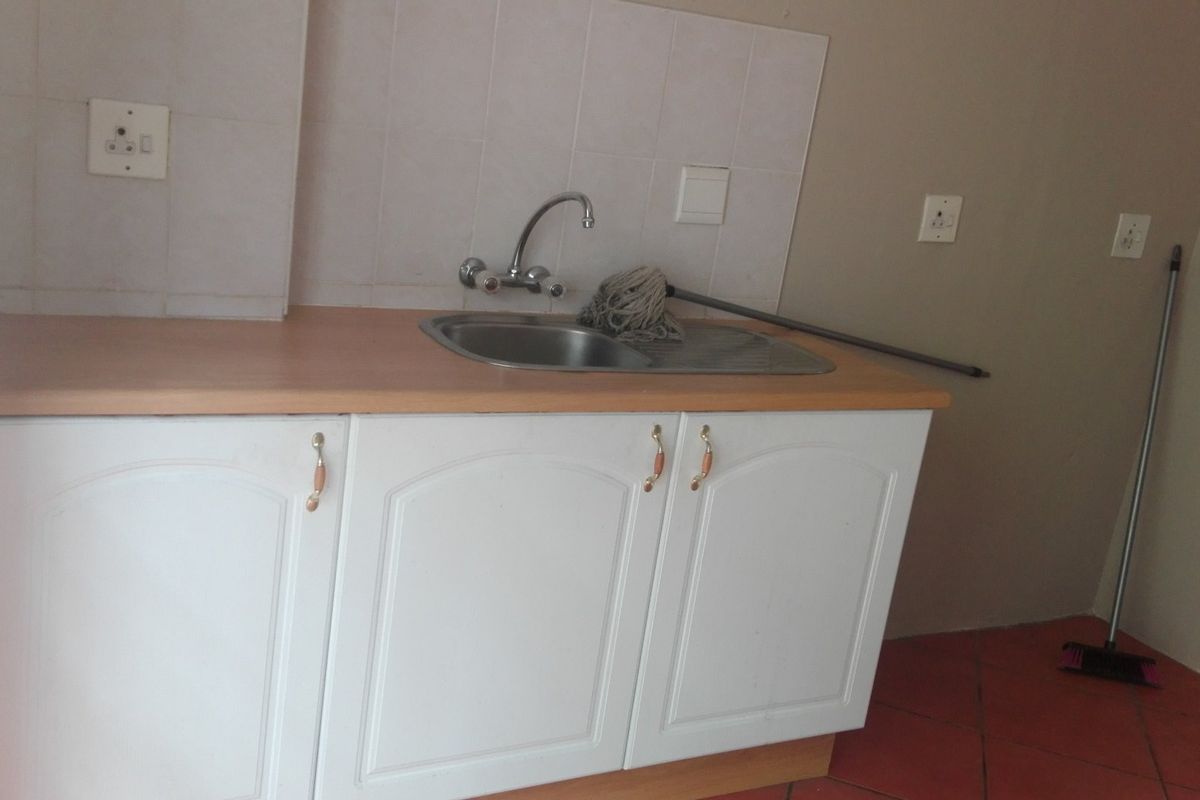 A functional kitchen area featuring white cabinetry, a stainless steel sink with mixer tap, laminate countertops, and terracotta floor tiles.