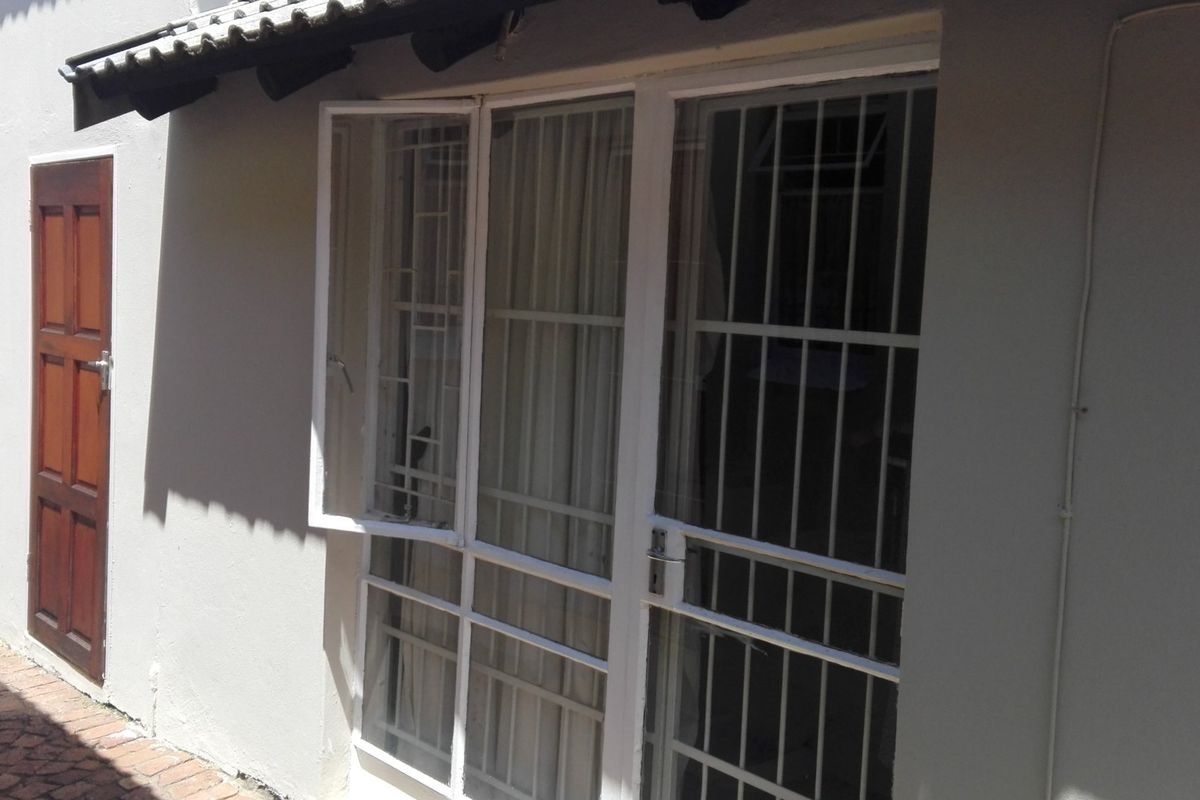Exterior view of the rear facade featuring a timber door, white framed glass doors with security bars, and brick paved walkway.