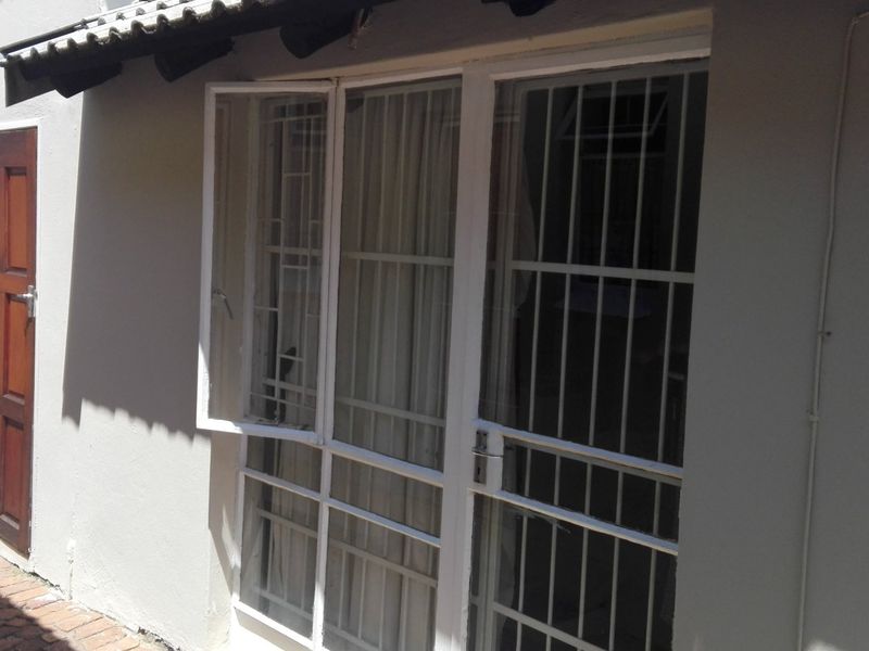 Exterior view of the rear facade featuring a timber door, white framed glass doors with security bars, and brick paved walkway.