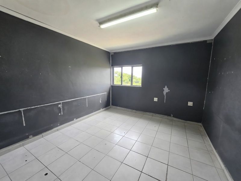 An empty office space featuring tiled flooring, dark painted walls with visible surface wear, and a single window providing natural light.