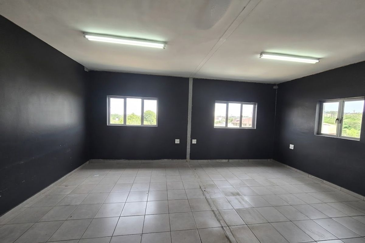An empty commercial office space featuring dark painted walls, tiled flooring, and multiple windows providing natural light.