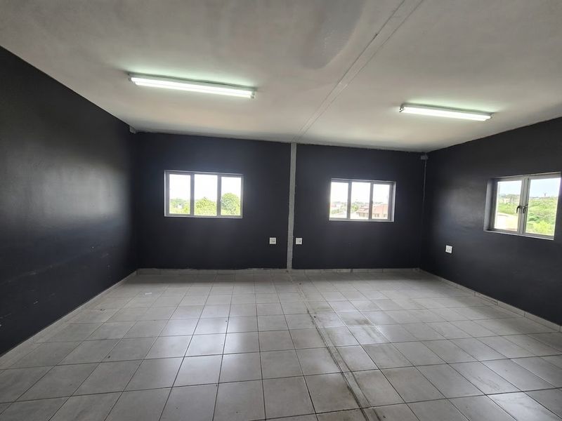 An empty commercial office space featuring dark painted walls, tiled flooring, and multiple windows providing natural light.