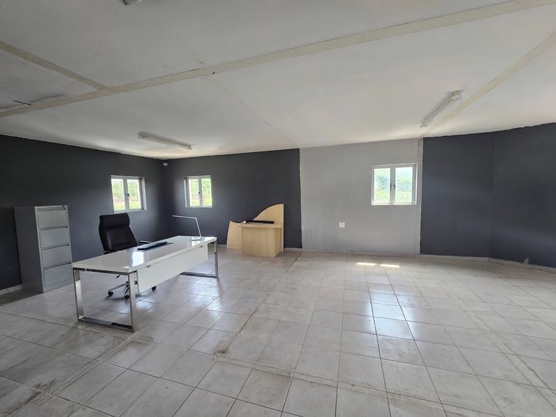 A spacious commercial office area featuring tiled flooring, fluorescent lighting, and multiple windows, providing a functional workspace with potential for cosmetic updates.