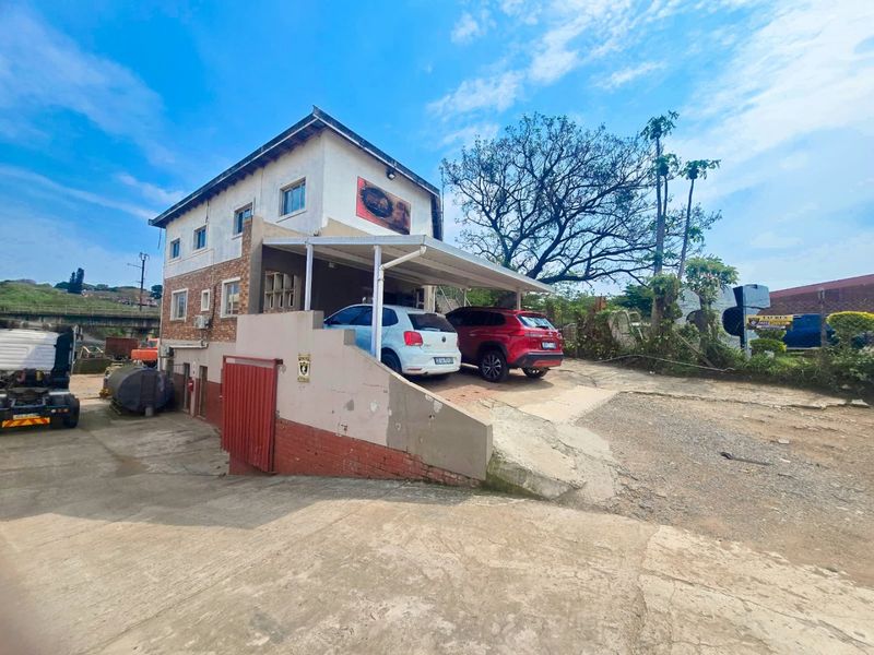 Commercial property exterior featuring a multi-level building with a covered parking area and concrete driveway access.