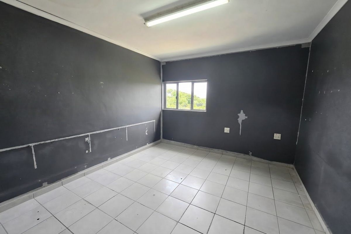 An empty office space featuring tiled flooring, dark painted walls with visible surface wear, and a single window providing natural light.