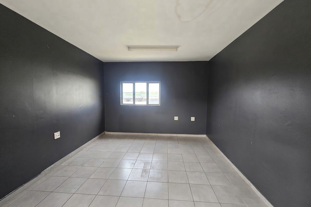 An empty office space featuring dark painted walls, tiled flooring, and a central window, suitable for a variety of commercial business applications.
