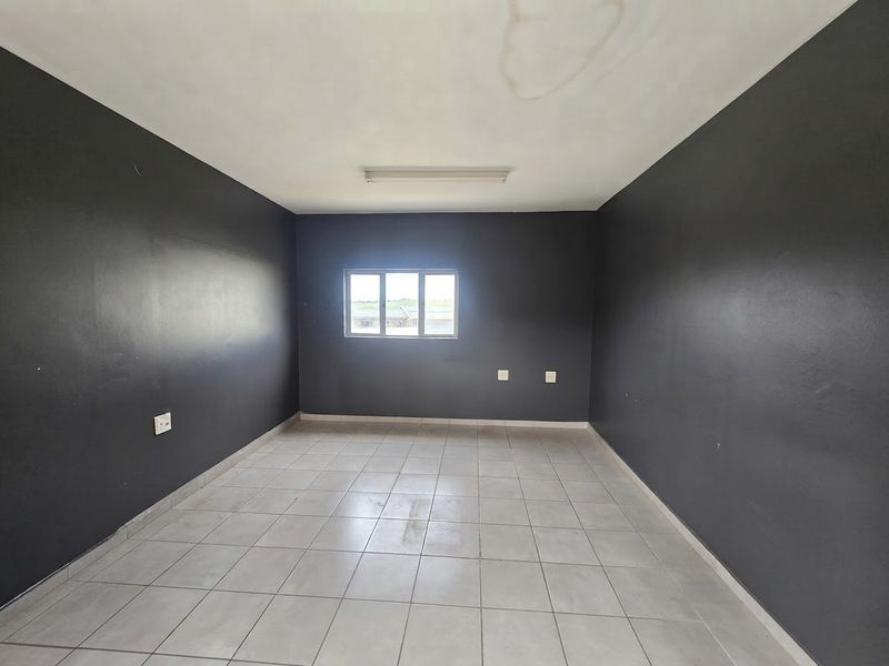 An empty office space featuring dark painted walls, tiled flooring, and a central window, suitable for a variety of commercial business applications.