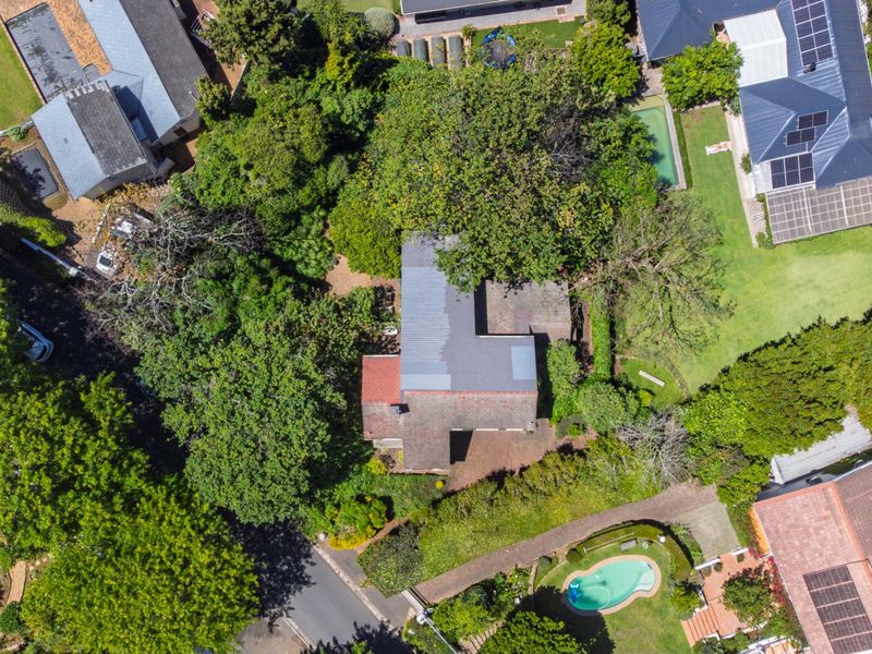 Aerial view of a residential property featuring a tiled roof, established garden, mature trees, and a private swimming pool.