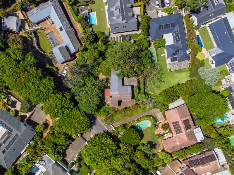 An aerial view of a residential neighborhood featuring multiple homes with swimming pools, solar panels, and mature garden landscaping.