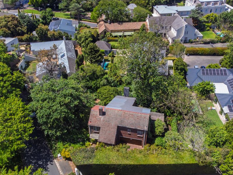 An aerial view of the property showcasing the roof structure, chimney, and surrounding mature garden within a leafy residential neighborhood.