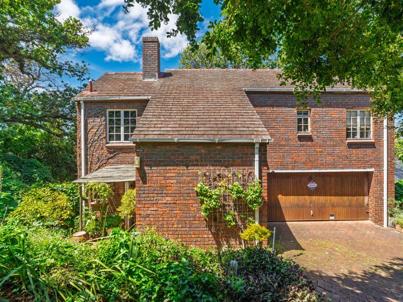 A charming double-story brick residence featuring a classic tiled roof, integrated garage, and established garden surroundings.