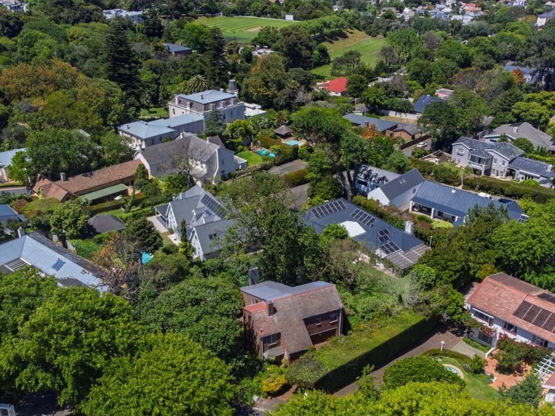 An aerial view of a lush, green residential neighbourhood featuring various homes with tiled roofs, solar panels, and established gardens.