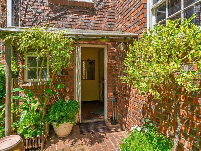 A charming rear entrance featuring exposed brickwork, a timber pergola, and brick-paved patio area.