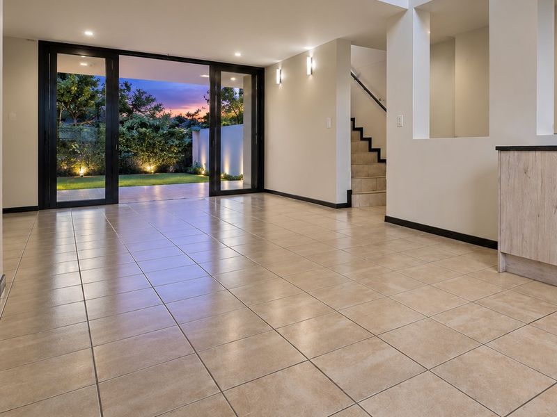 Spacious open-plan living area featuring neutral tiled flooring, modern built-in cabinetry, and large sliding glass doors opening to a landscaped garden.