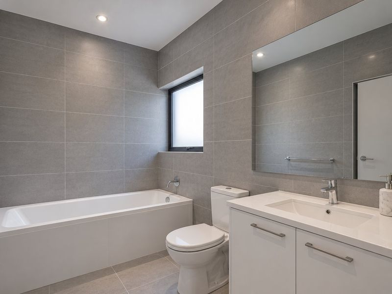 Modern bathroom featuring floor-to-ceiling grey tiling, a built-in bathtub, a sleek vanity with integrated sink, and a large wall mirror.