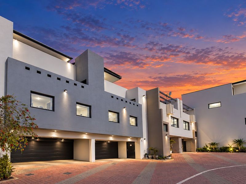 Modern multi-level residential facade featuring a paved driveway, integrated double garages, and contemporary architectural design at dusk.