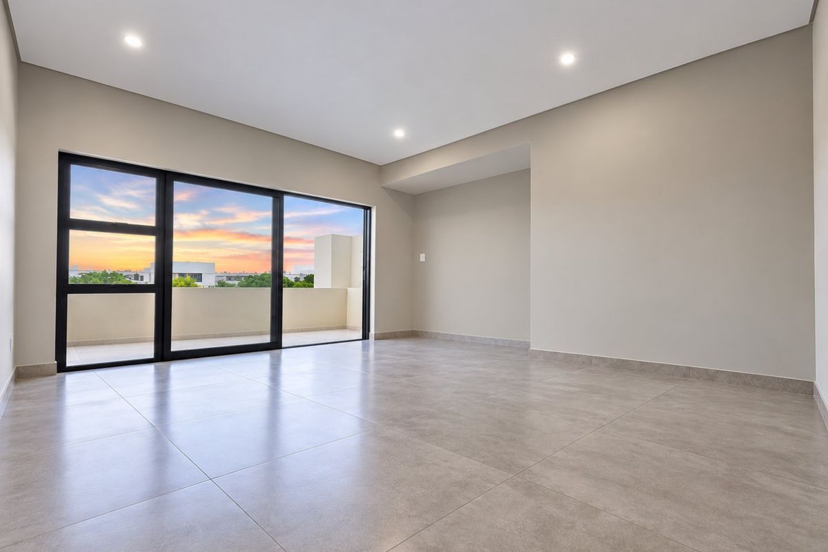 A bright, modern, and spacious living area featuring large sliding glass doors that open onto a balcony, finished with neutral tiles and recessed lighting.