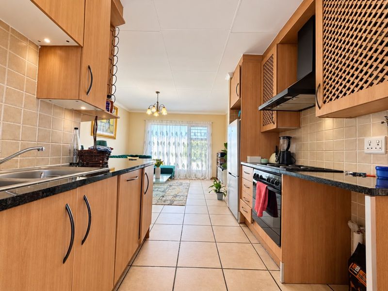 Open-plan kitchen featuring wood-finish cabinetry, granite-look countertops, and integrated appliances, flowing seamlessly into a bright living area with large windows.