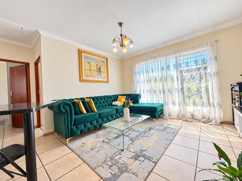 A bright and well-maintained living room featuring tiled flooring, a decorative ceiling light, and large windows fitted with security bars.