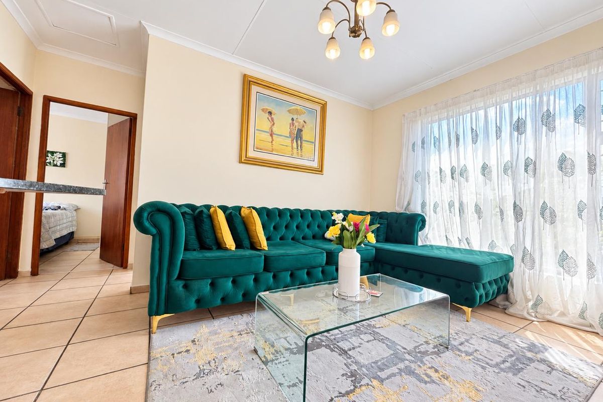 A bright and well-maintained living room featuring neutral tiled flooring, coved ceilings, and a classic multi-arm chandelier, offering a comfortable and inviting atmosphere.