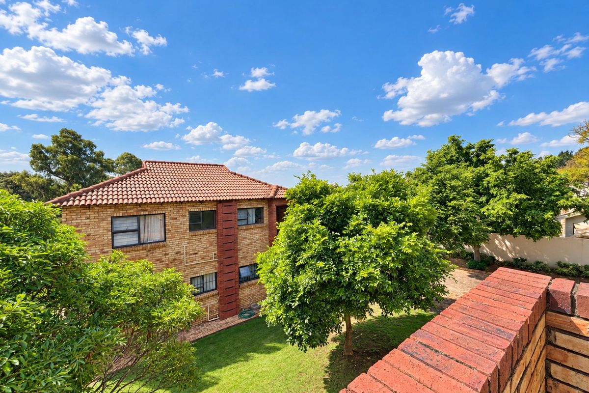 A view of the rear exterior of the apartment building, featuring face brick construction, a tiled roof, and a well-maintained garden area.